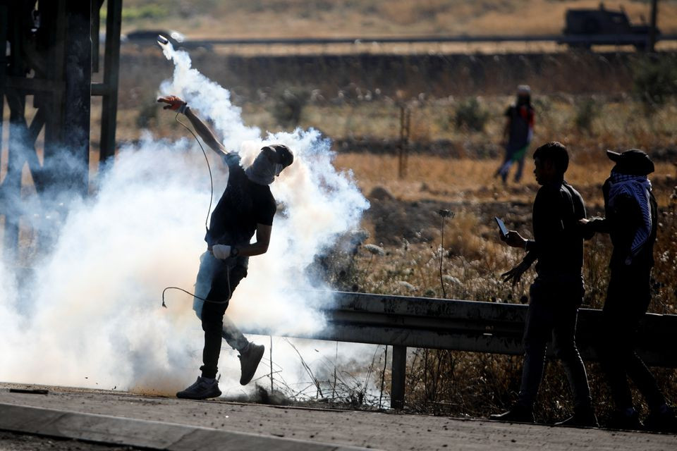 A Palestine protestor throws back a tear gas grenade during an anti-Israel protest over cross-border violence between Palestinian in Gaza and the Israeli military, near Hawara checkpoint near Nablus in the Israeli-occupied West Bank, May 18, 2021. PHOTO: REUTERS