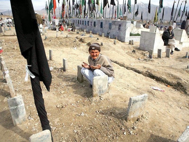 a male member of the hazara community prays at his relatives graves at a cemetery a hazara girl below sells old school bags along a road stall while she waits for customers in quetta photo reuters