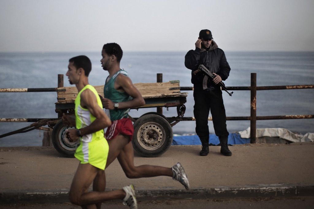a picture taken on may 5 2011 shows a hamas policeman talking on the phone as palestinian olympic athlete nader masri l and a fellow runner speed along the waterfront in gaza city as they compete in the gaza strip 039 s marathon