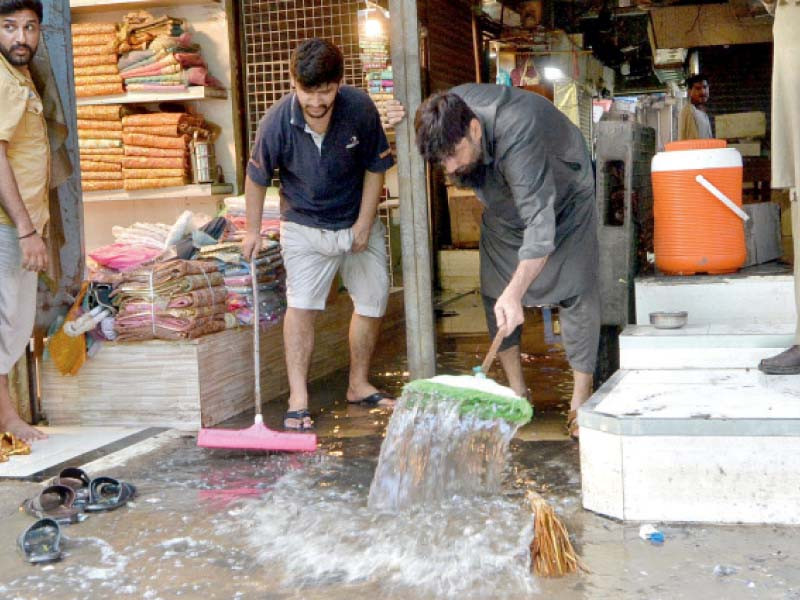 shopkeepers clean rainwater from a market on the first working day after eid holidays photo jalal qureshi express