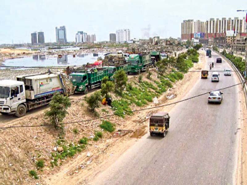 dumper trucks are parked along shaheed e millat expressway near the garbage station on the malir river bank rising water levels have made movement of tonnes of garbage impossible photo express