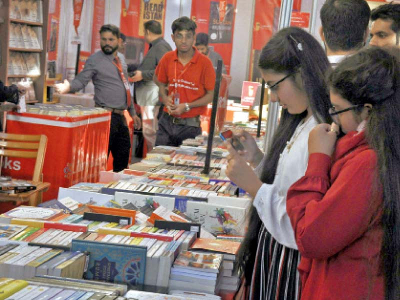 people browse through books at a discount stall while panelists of the inaugural session take the stage at the 14th karachi literature festival photos agencies file