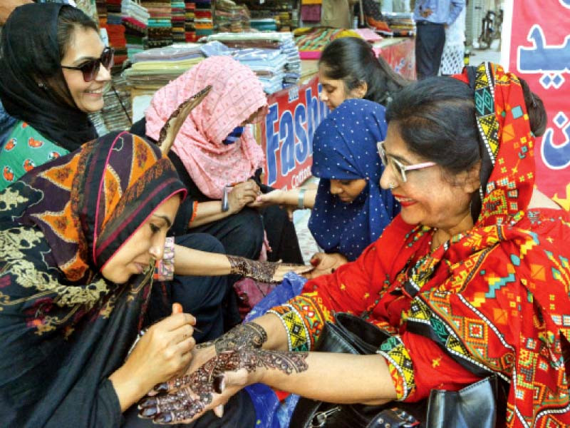 women share a light moment as they get henna designs on their hands at one of the temporary stalls set up in front of shopping malls in clifton near teen talwar intersection women making intricate designs of mehndi charge at least rs400 per hand photo jalal qureshi express