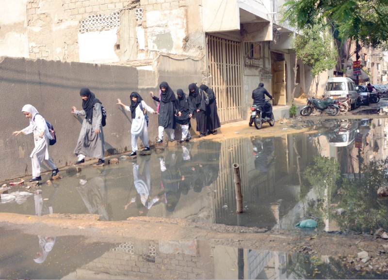 girls try to cross a street without getting their feet in the overflowing sewage from a choked gutter in the akhtar colony neighbourhood photo jalal qureshi express