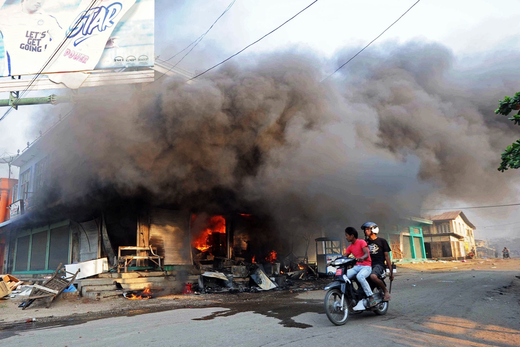 residents ride a motorcycle past a burning building in riot hit meiktila central myanmar on march 22 2013 photo afp