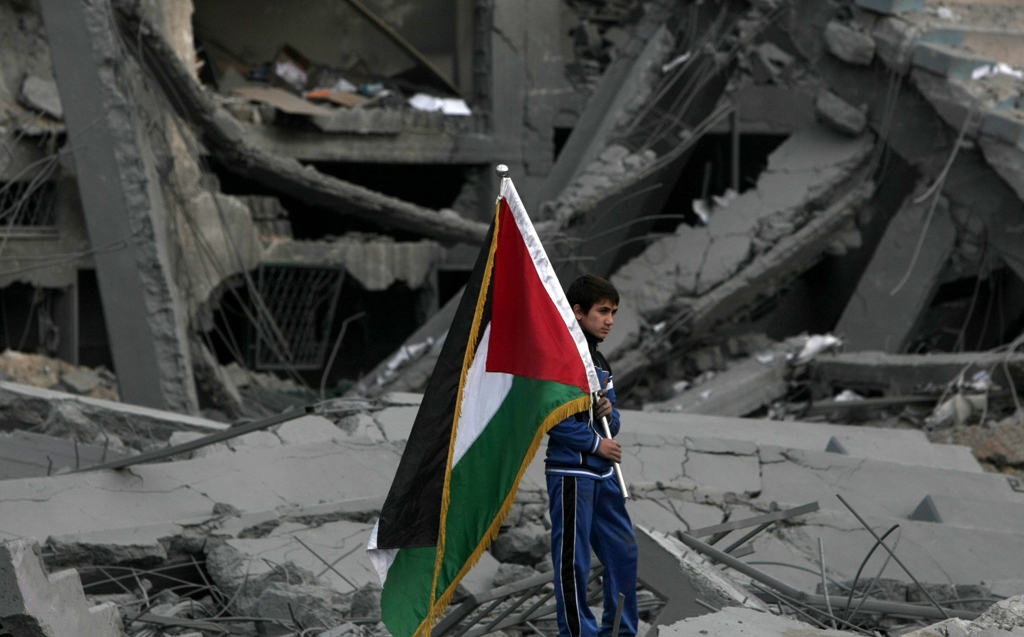 a palestinian boy carries the national flag as he makes his way through the debris of the destroyed palestine sports stadium in gaza city on november 22 2012 after a ceasefire took hold in and around gaza after a week of cross border violence between israel and palestinian militants that killed at least 160 people photo afp