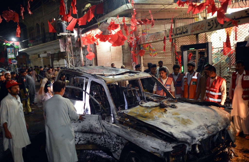 local residents and volunteers gather around a destroyed vehicle at the site of a suicide bomb attack at an election campaign rally in peshawar on april 16 2013 photo afp