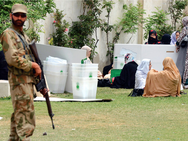 election officials are guarded by a soldier as they sit with their ballot boxes while awaiting transport at a distribution centre in quetta photo afp