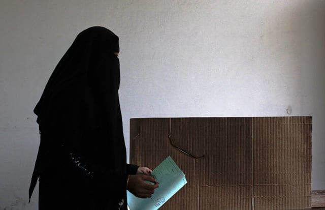 a woman voter holds her ballot paper and stamp while moving to a polling booth inside a polling station on may 11 2013 photo reuters