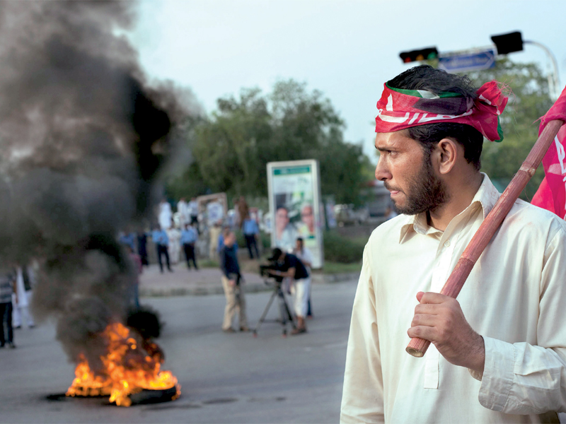 a pti supporter walks past burning tyres during the protest photo myra iqbal express