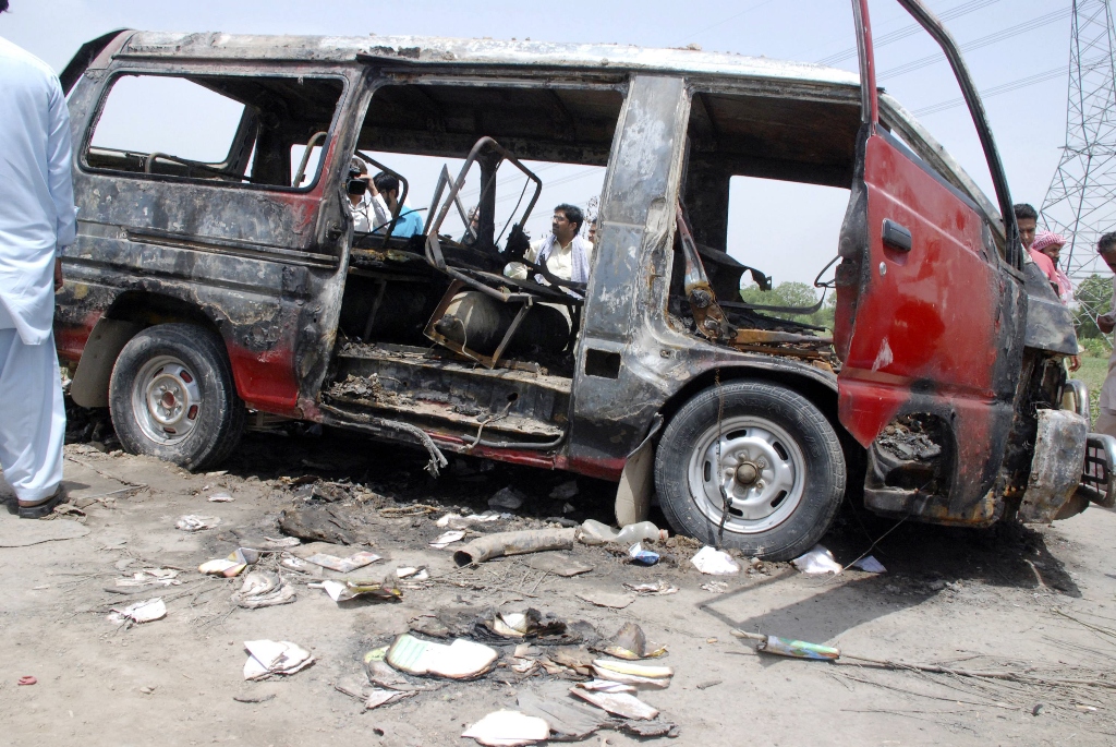 men stand around a burnt out school bus after a gas cylinder on it exploded killing seventeen children on the outskirts of gujrat photo reuters