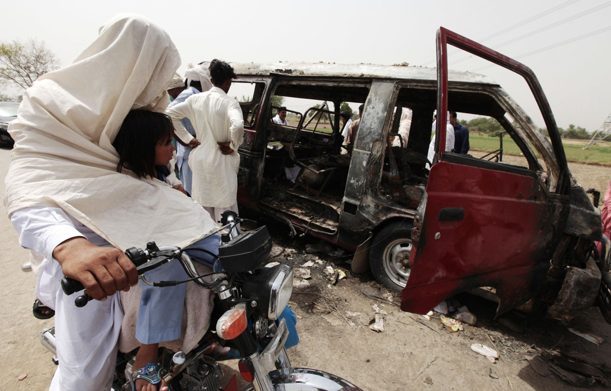 a man and his daughter ride a motorcycle past a burnt out school bus after a gas cylinder on it exploded killing seventeen children on the outskirts of gujrat photo reuters