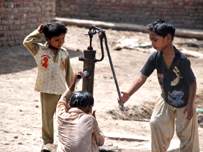 a boy helps his friend bathe in the water from a hand pump as the mercury continues to rise in upper sindh yet power outages worsen photo naeem ghouri express