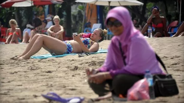 a muslim woman wearing a veil sits in front of foreign tourists wearing bikinis on kuta beach in bali june 6 2013 photo afp a muslim woman wearing a veil sits in front of foreign tourists wearing bikinis on kuta beach in bali june 6 2013 photo afp