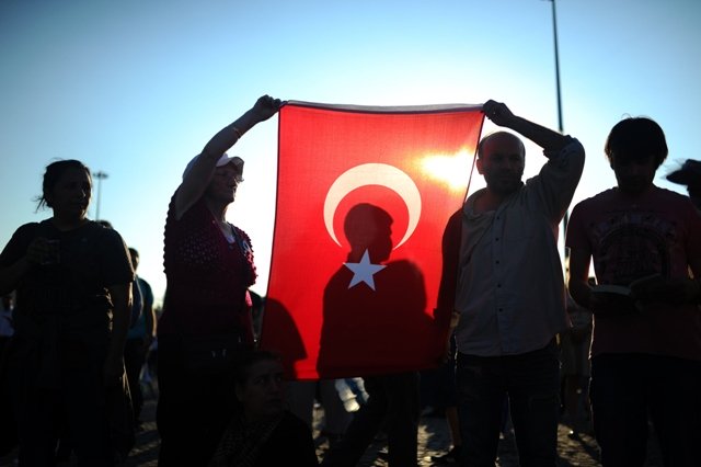 people hold a turkish national flag as they stand on the flashpoint taksim square in istanbul on june 18 2013 during a wave of new alternative protests photo afp