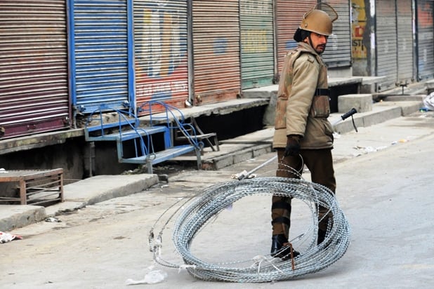 an indian policeman drags razor wire to be used to block a street during a curfew in srinagar on february 9 2013 photo afp