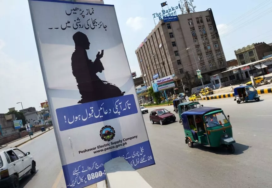 commuters ride past a poster from the electric supply company in peshawar on july 21 2013 photo afp commuters ride past a poster from the electric supply company in peshawar on july 21 2013 photo afp