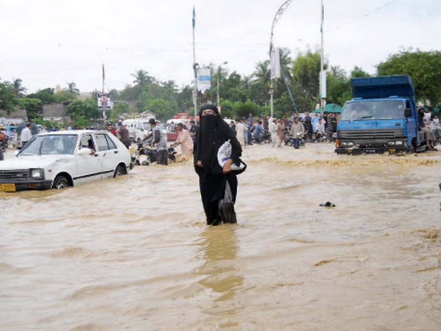 the torrential rain in the city has caused a lot of inconvenience for the citizens a woman is seen trying to walk through a road submerged in rainwater at kda chowrangi photo mohammad noman express