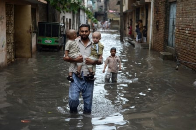 a pakistani man carries young children along a flooded street after the heavy rain in rawalpindi photo afp a pakistani man carries young children along a flooded street after the heavy rain in rawalpindi photo afp