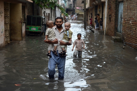 a pakistani man carries young children along a flooded street after the heavy rain in rawalpindi photo afp
