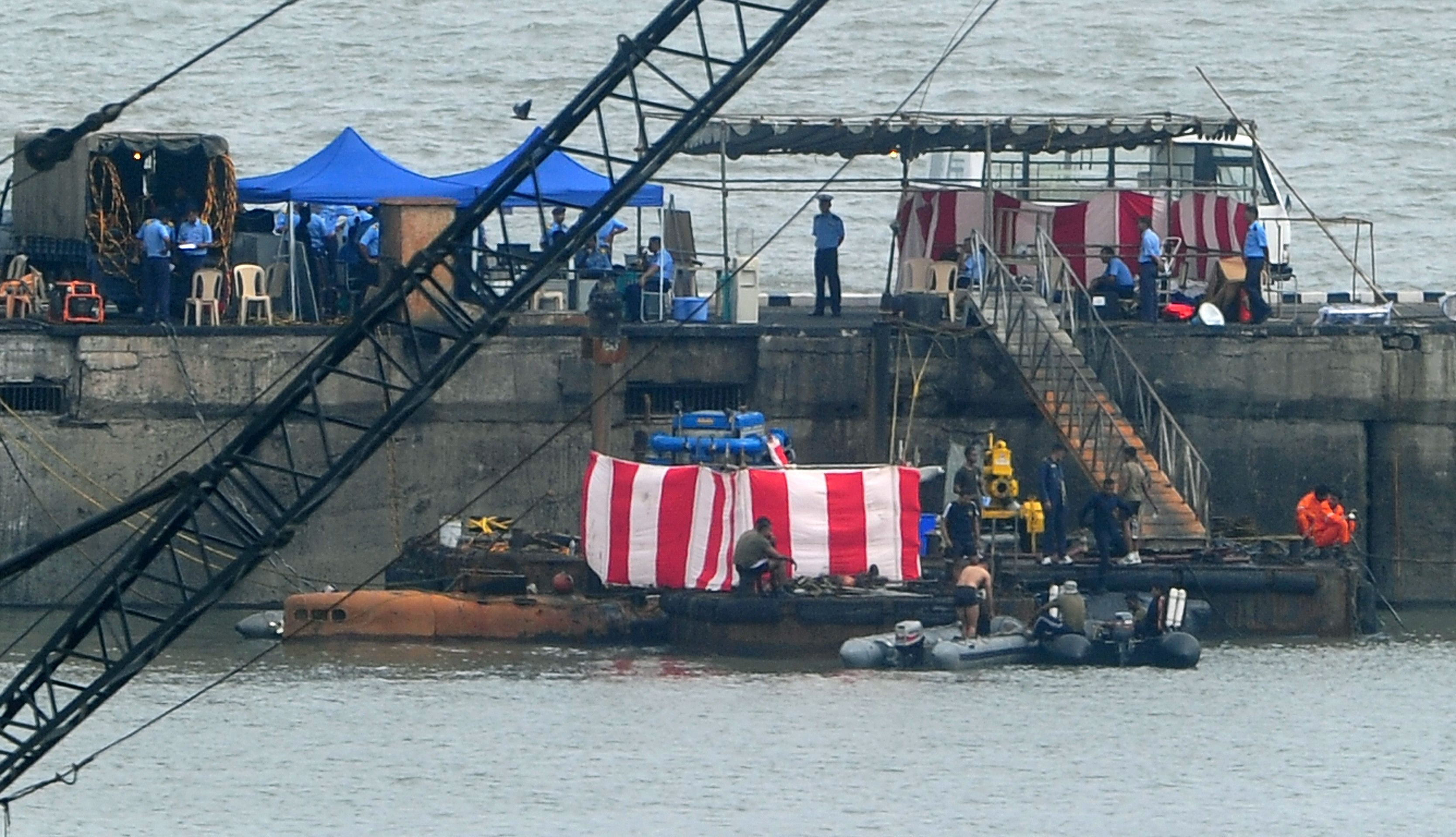 indian navy divers are seen on board an inflatable craft next to the conning tower of diesel powered ins sindhurakshak covered with red and white sheet as it lies submerged inside the naval dockyard in mumbai photo afp