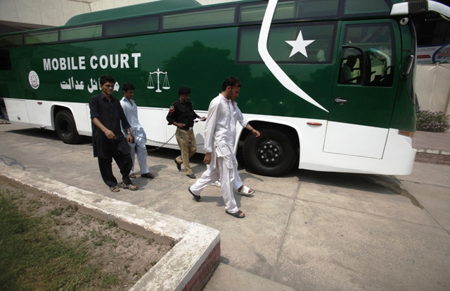 a policeman escorts men who will be appearing before the first mobile court which is set up inside a bus in hayatabad peshawar august 27 2013 photo reuters