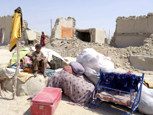 a young boy sits on his belongings beside his collapsed mud house at labch area in the earthquake devastated district of awaran photo afp