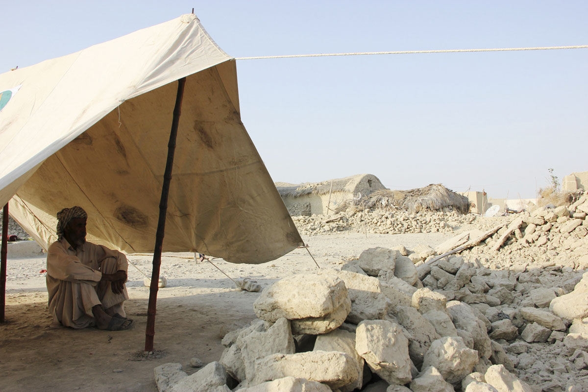 an earthquake survivor sits in a makeshift tent near the rubble of mud houses which collapsed following the quake in awaran in balochistan photo reuters