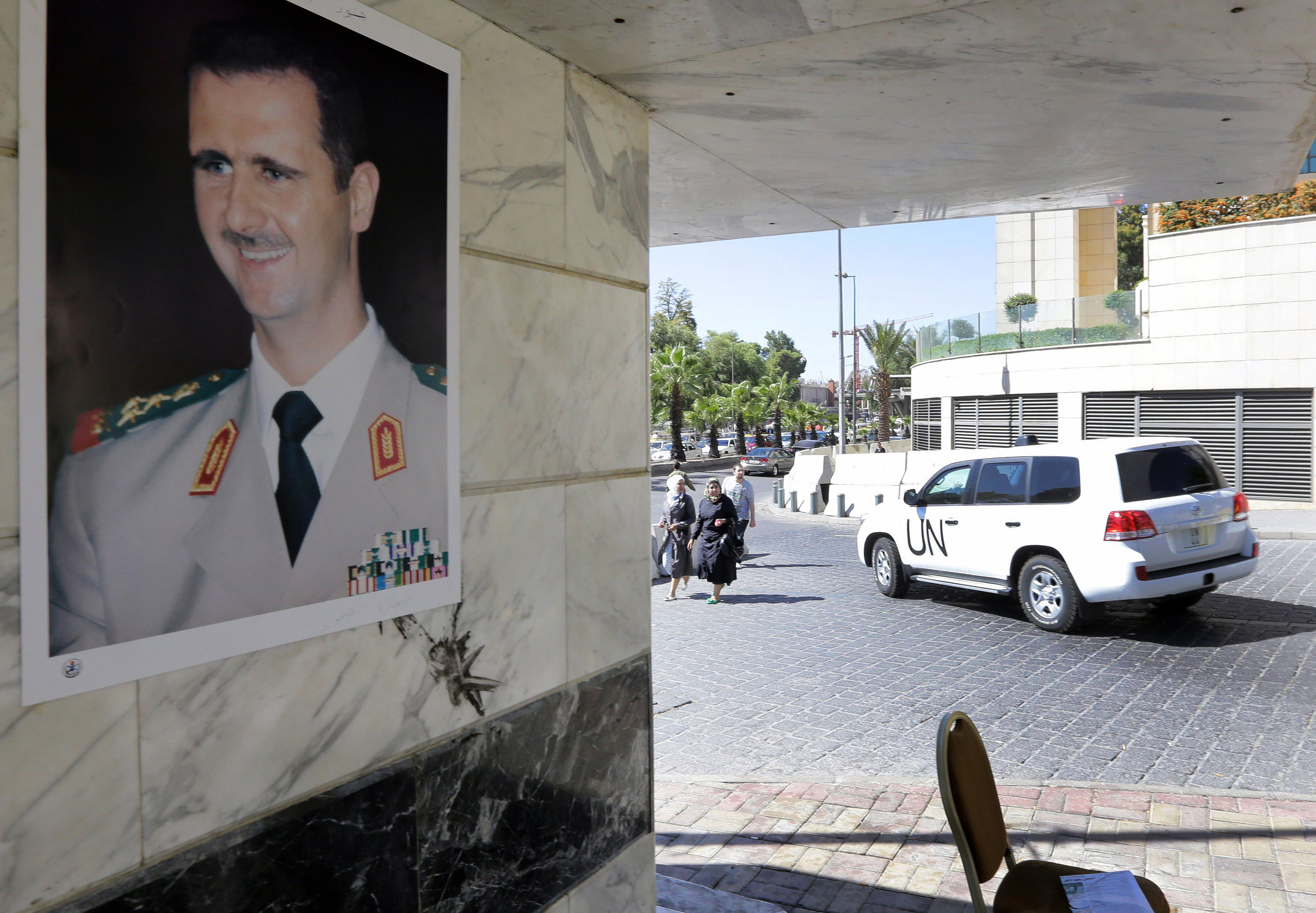 a poster of syrian president bashar al assad adorns a wall as a united nations vehicle carrying inspectors from the organisation for the prohibition of chemical weapons opcw leaves a hotel in damascus on october 9 2013 photo afp