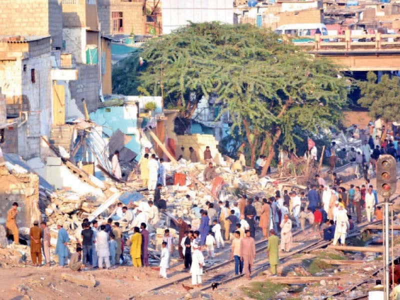 people stand near their illegally built homes which were demolished by the authorities on wednesday along the railway tracks in the kala pull area of karachi photo jalal qureshi express