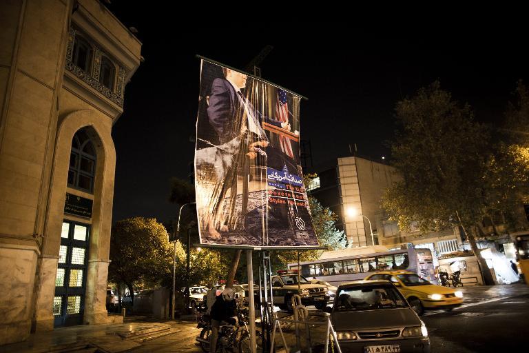 an anti american poster depicting an american negotiator sitting at a negotiating table with a dog on his side is displayed next to a mosque in downtown tehran on october 27 2013 photo afp