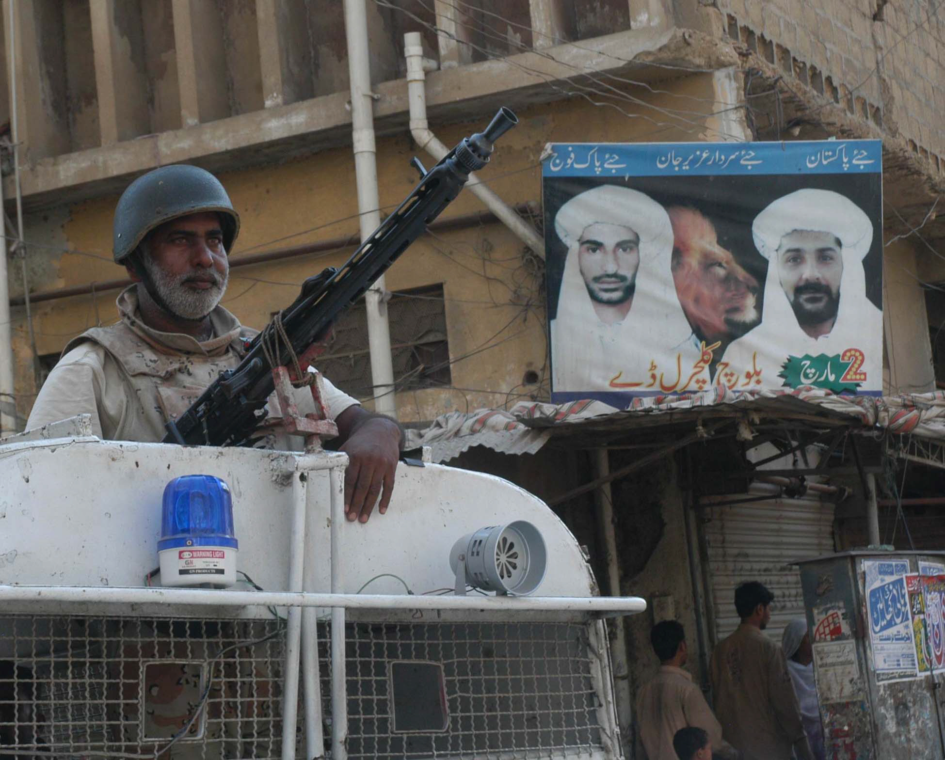 a ranger stands watch armed with a machine gun in lyari with a poster bearing the photo of uzair jan baloch wanted by the law in the background photo rashid ajmeri express