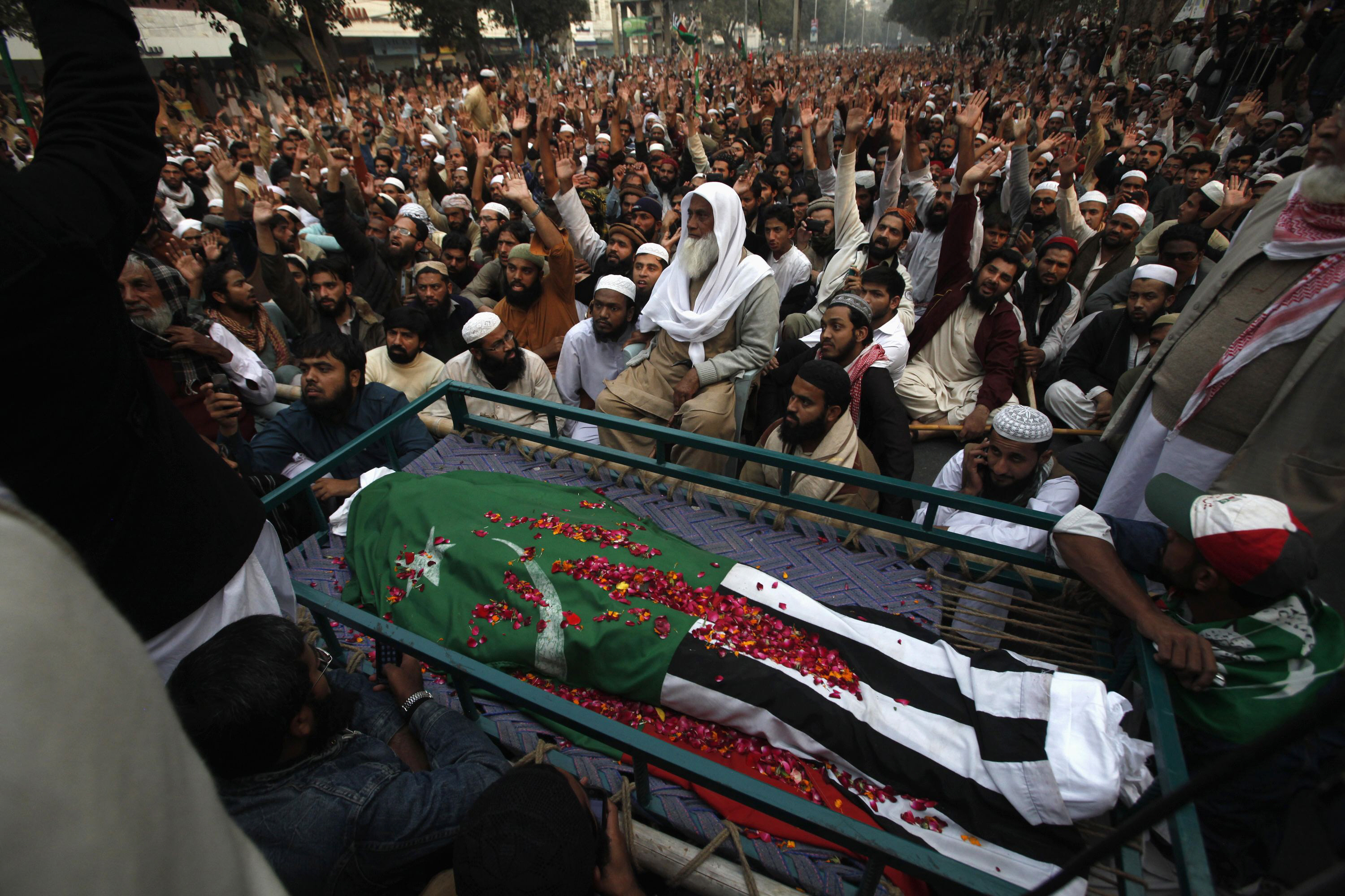 supporters of ahl i sunnat wal jamaat aswj sit near the body of their party leader maulana shamsur rehman wrapped in the party 039 s flag while shouting slogans during a funeral procession in lahore december 7 2013 photo reuters