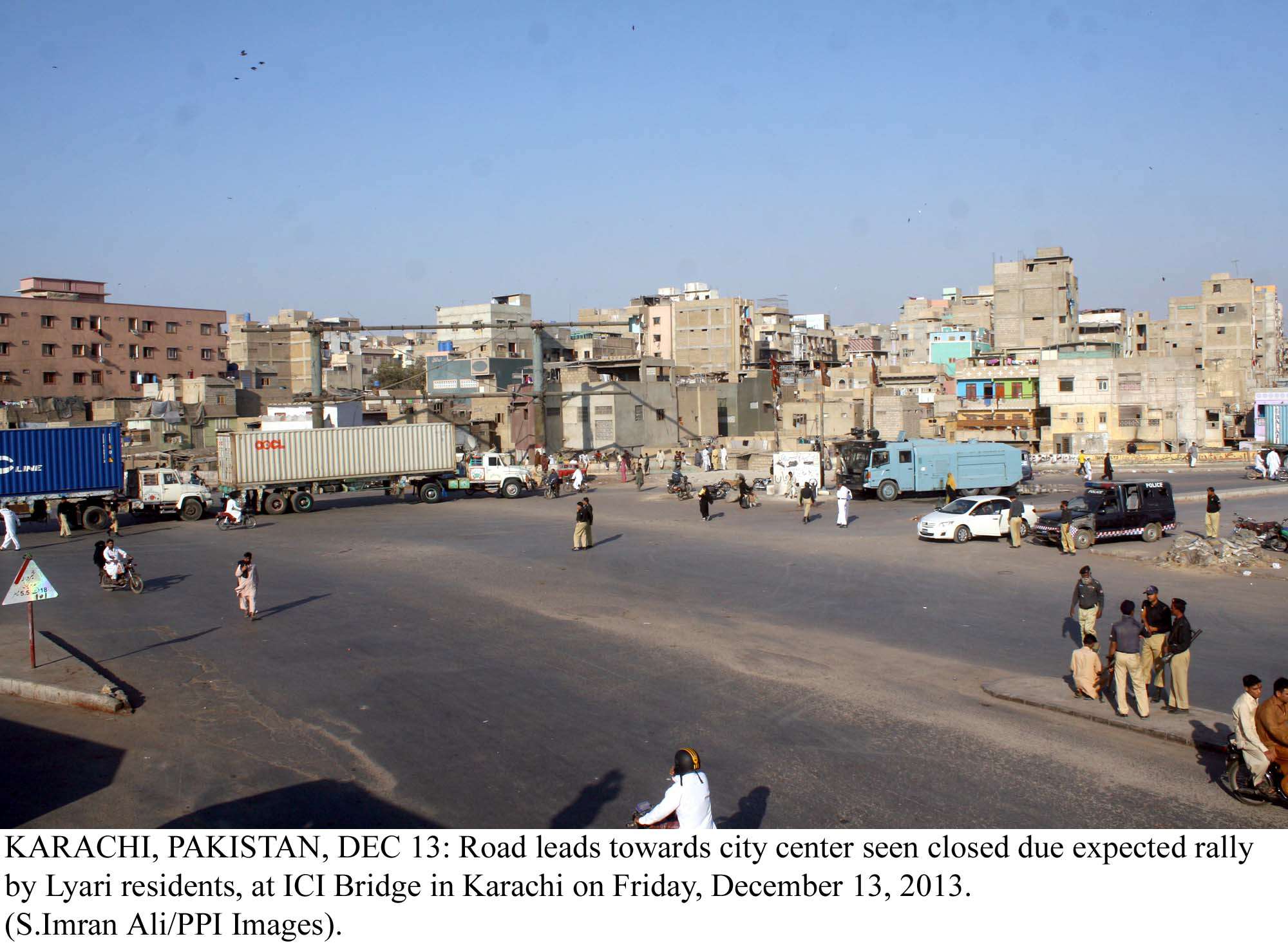 police officials and riot control vehicles stand alert as a road leading from lyari to the city centre is blocked with trailers on friday photo ppi