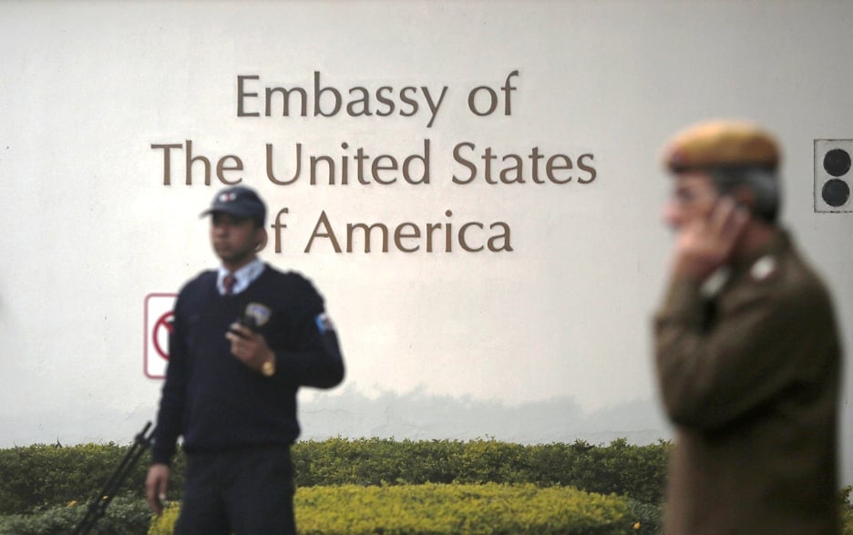 a u s embassy security guard l and an indian policeman stand in front of the main gate of the embassy as the bulldozer unseen removes the security barriers in new delhi december 17 2013 photo reuters