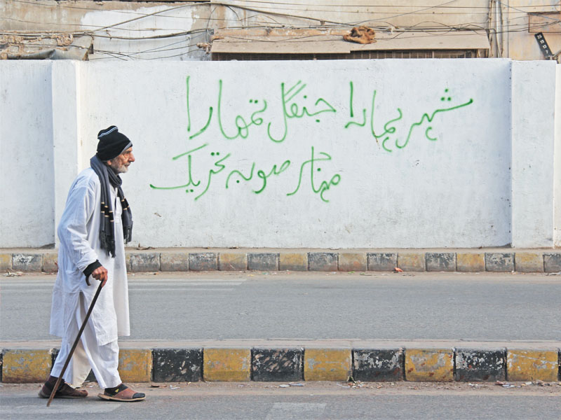 a man walks in front of a wall painted with a slogan demanding a separate province in gulshan e iqbal photo ayesha mir express