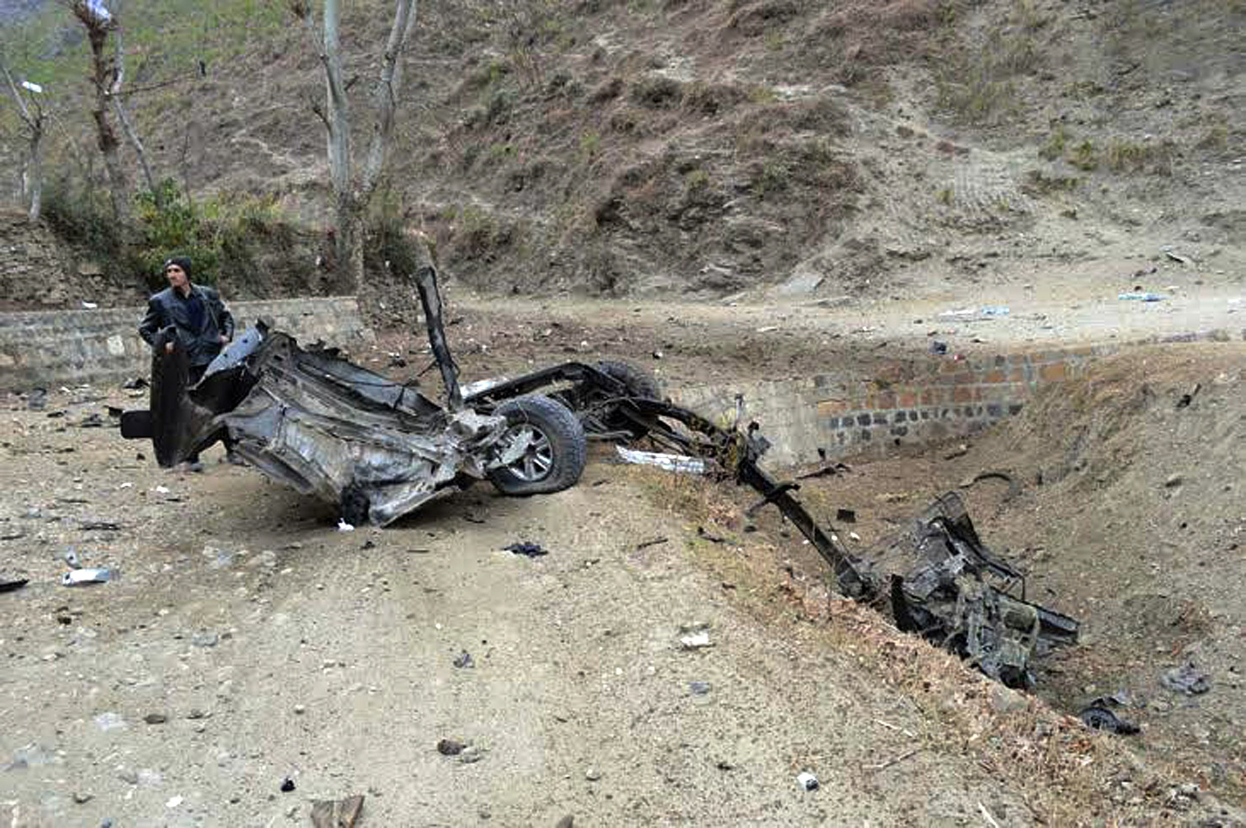 a policeman stands beside the wreckage of a destroyed police vehicle after a roadside bomb explosion targeting amir muqam 039 s convoy in the martong area of swat valley on january 12 2014 photo afp