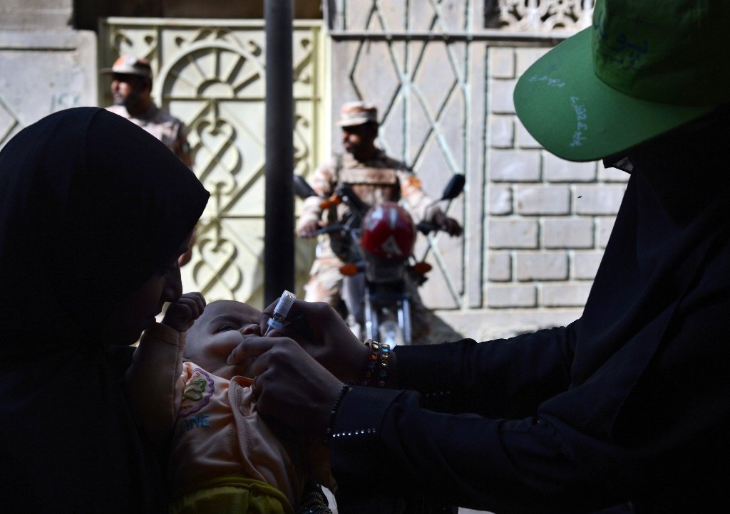 a pakistani polio vaccination worker administers polio vaccine drops to an infant as paramilitary soldiers stand guard photo afp file