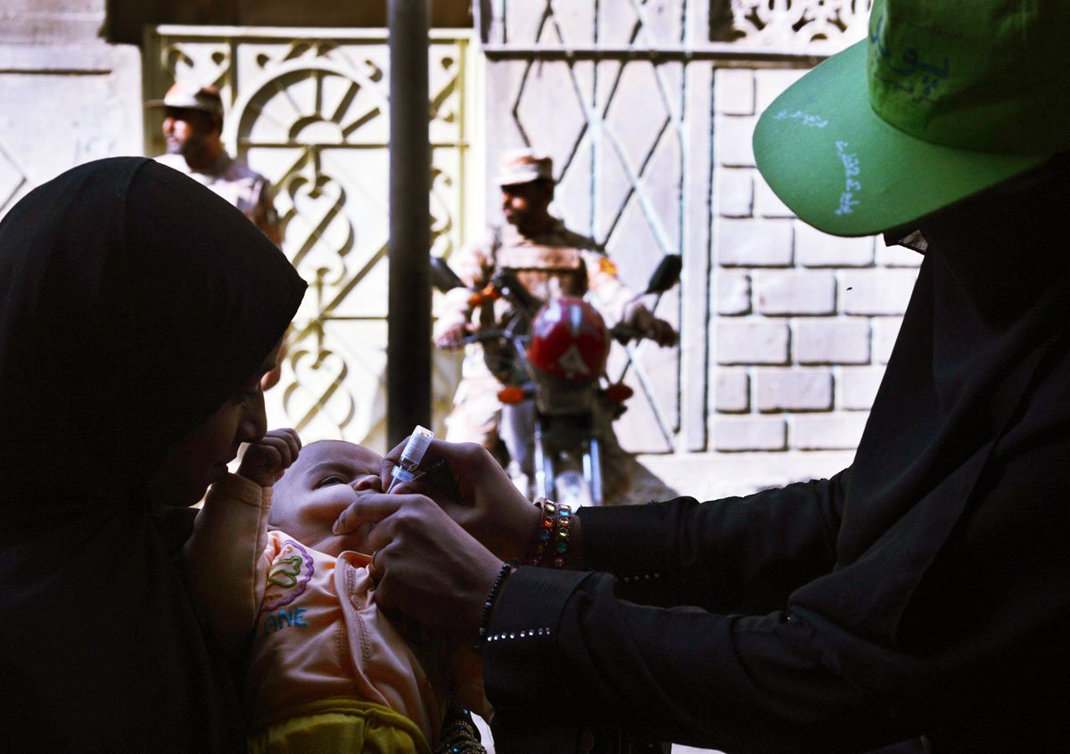 a polio vaccination worker administers polio vaccine drops to an infant as paramilitary soldiers stand guard photo afp file