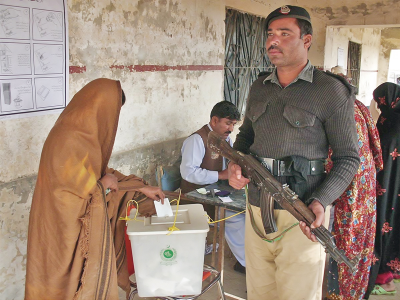 policeman stands alert as a woman casts vote during local government elections at union council nasirabad photo online