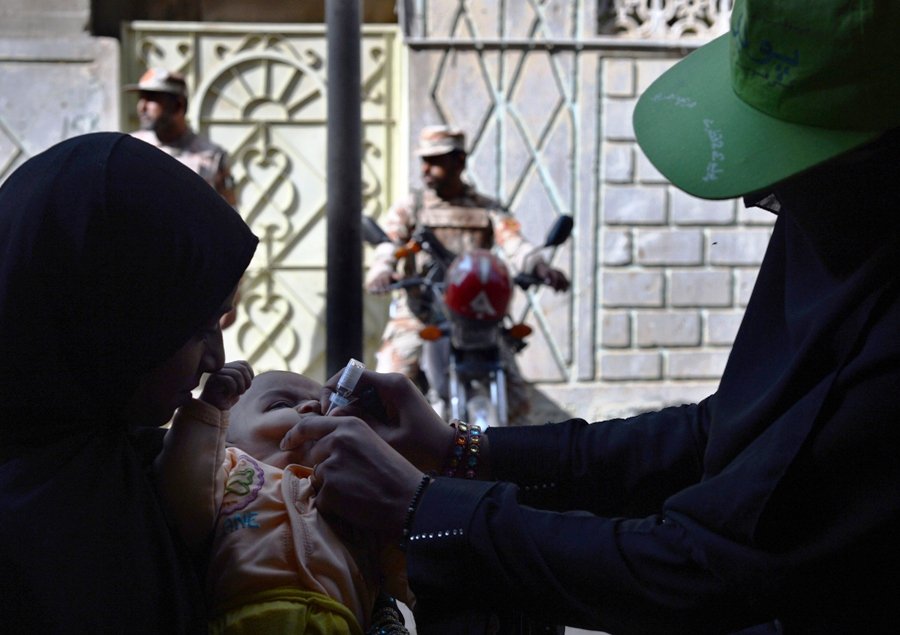 polio vaccination worker administers polio vaccine drops to an infant as paramilitary soldiers stand guard in karachi on january 8 2013 photo afp