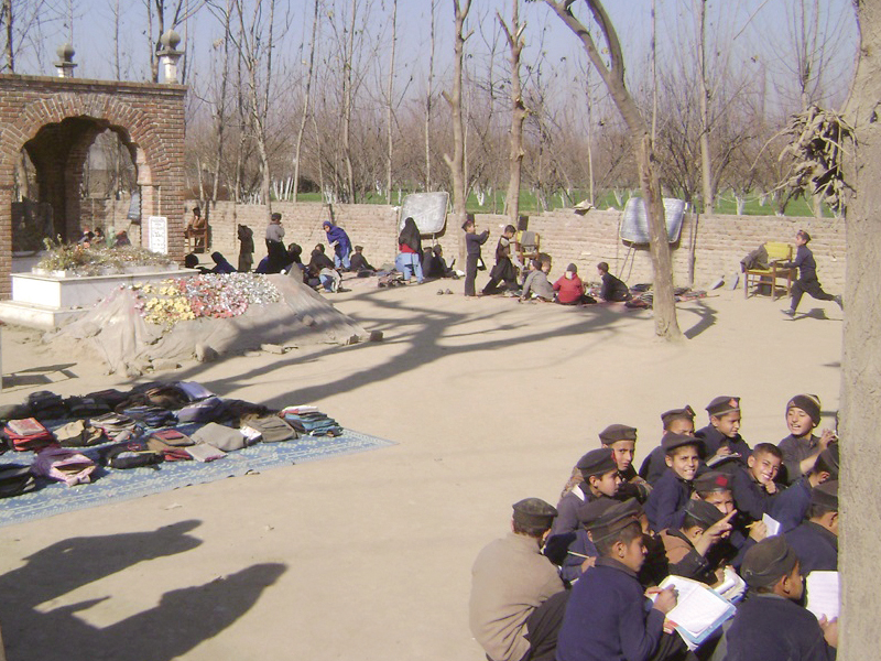 students sit on the ground next to a grave as they take their lessons under the open sky photo ahtisham khan express