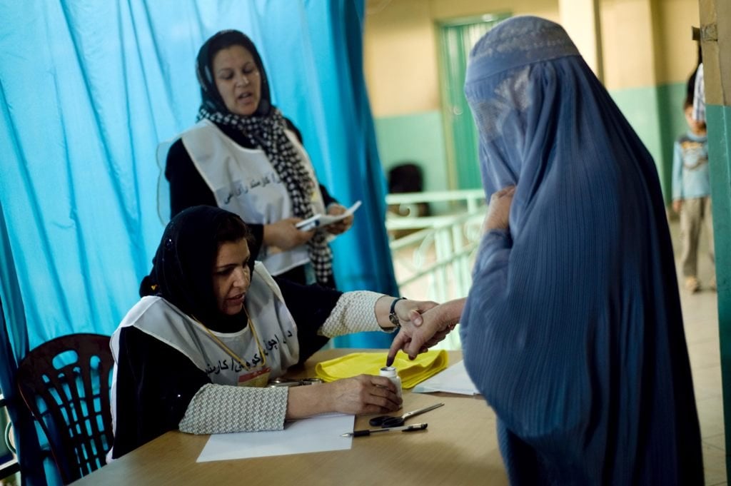 an electoral worker assists an afghan burqa clad woman as she inks her finger prior to voting inside a polling centre photo afp