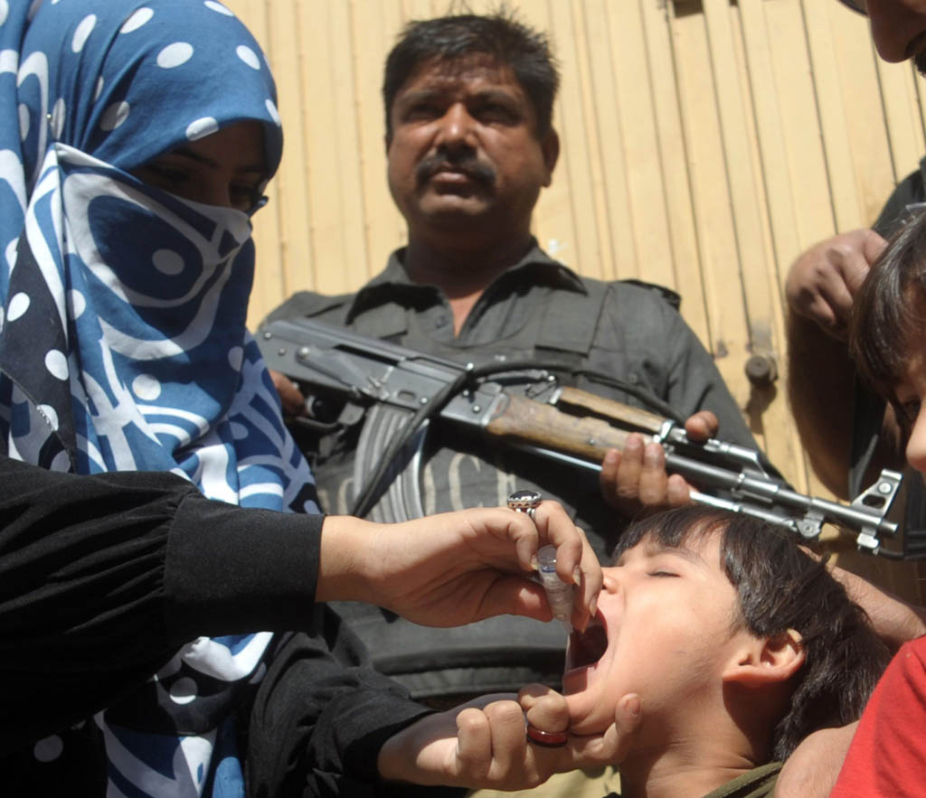 a policeman stands guard as a member of a polio vaccination team administers drops to a child during a door to door vaccination campaign in karachi photo afp file