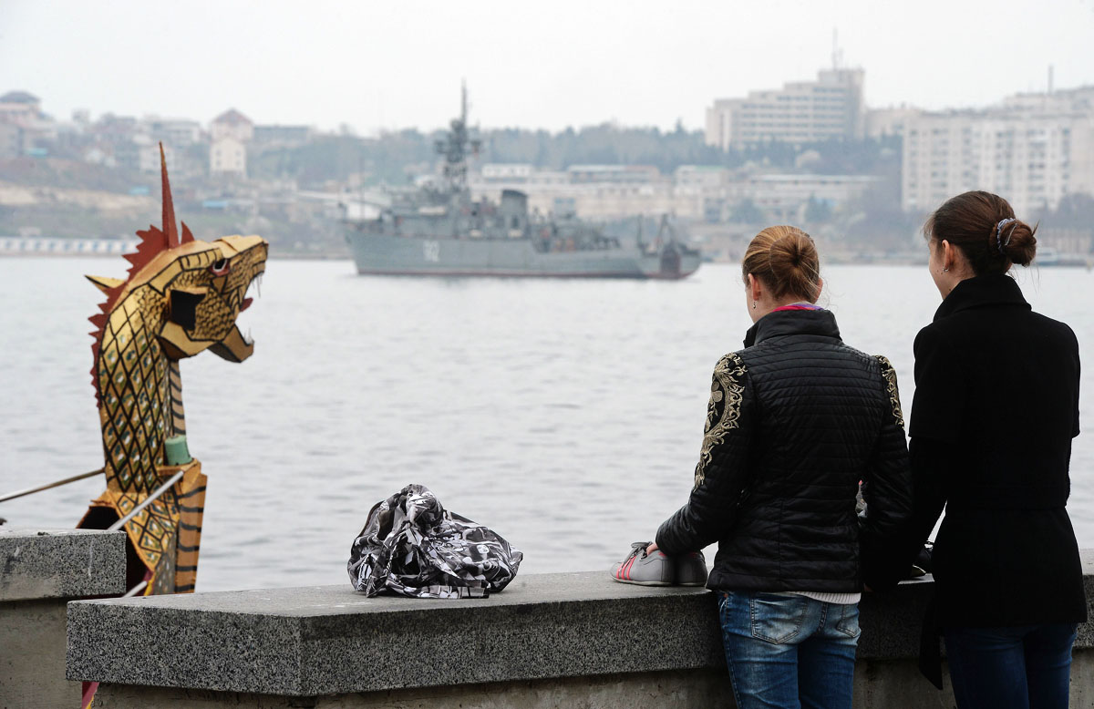 women stand on a seaside promenade with a tourist ship doced as the russian navy minesweeper ship quot turbinist quot guards the port of sevastopol in the crimean peninsula on march 8 2014 photo afp