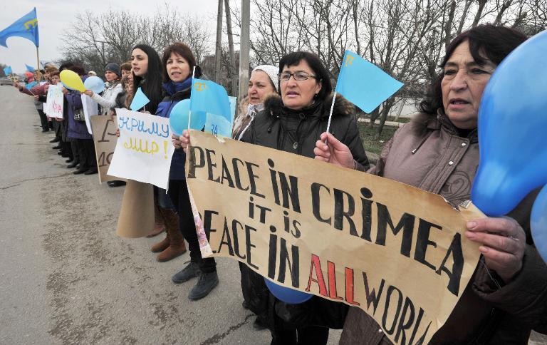 women hold crimean tatar flags and placards reading quot peace in crimea it is peace in all world quot during an anti war rally in simferopol on march 8 2014 photo afp