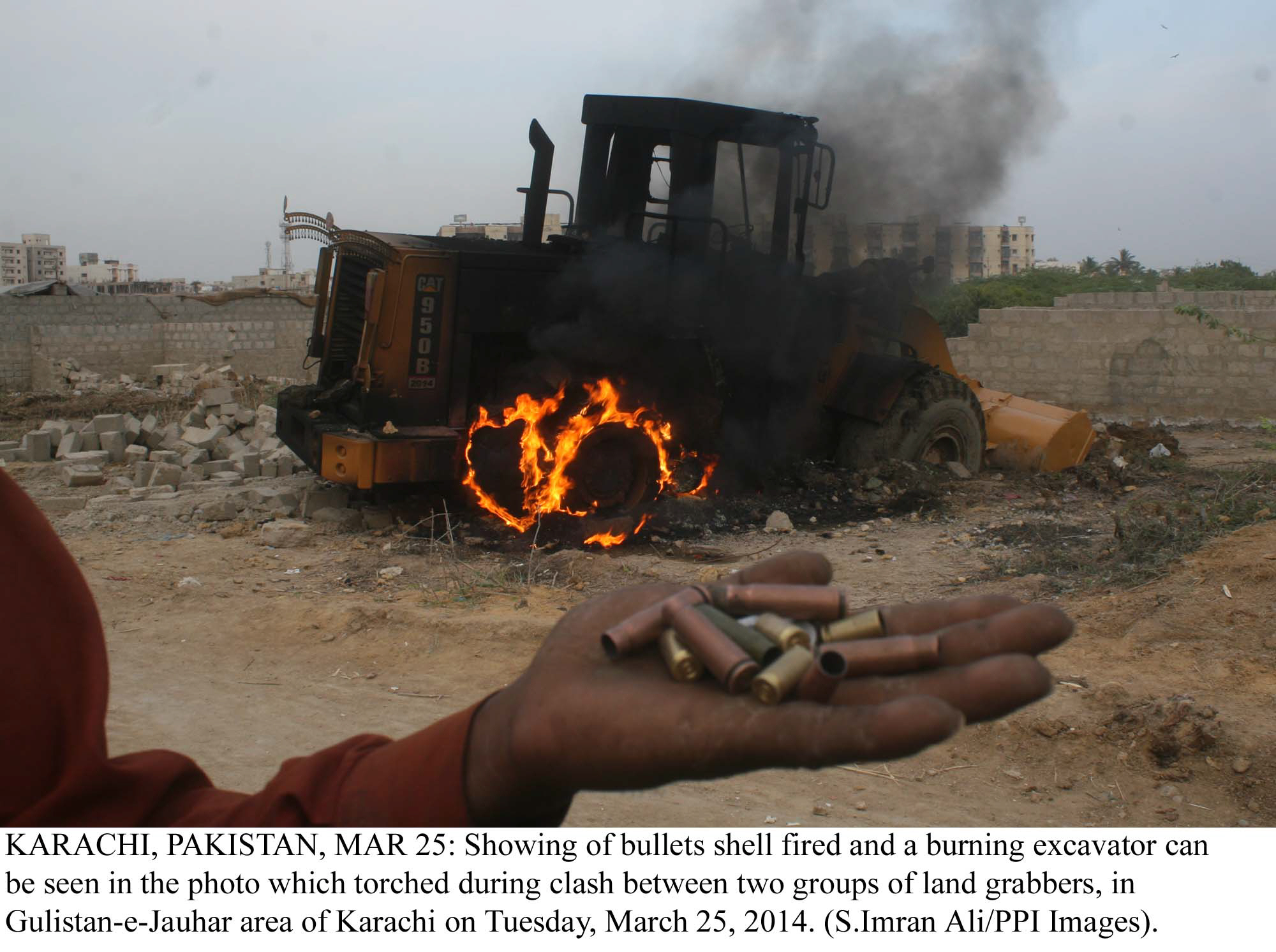 a man holds up casings of bullets which were fired into the air as a bulldozer burns in the background near the site of an anti encroach drive in gulistan e jauhar on tuesday