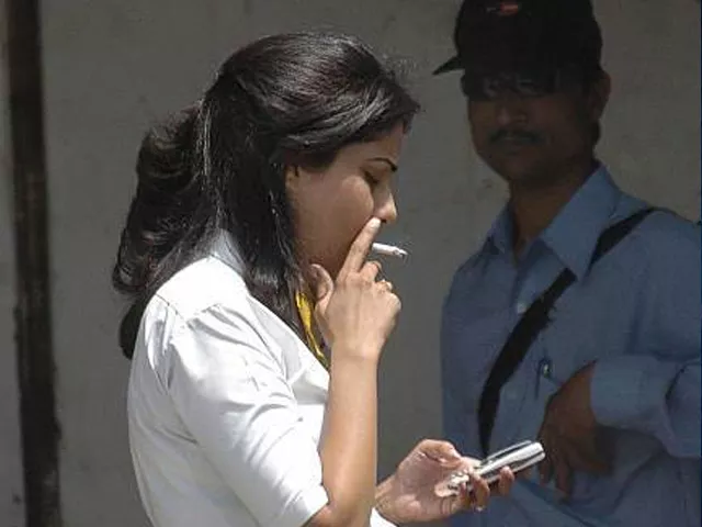 an indian woman l is watched by a security guard as she enjoys a cigarette while looking at her mobile telephone on a pavement in new delhi 03 may 2004 photo afp an indian woman l is watched by a security guard as she enjoys a cigarette while looking at her mobile telephone on a pavement in new delhi 03 may 2004 photo afp