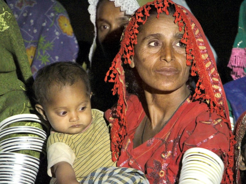 a thari mother with hope in her eyes stands in a queue holding her baby waiting to collect her bag of food photo manoj kumar