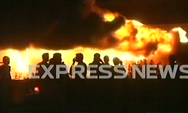 a screenshot of people standing near the bus that was set on fire by protesters